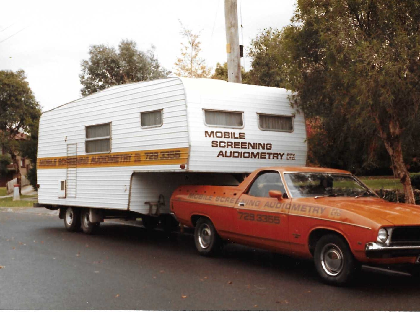 1982 Ford Falcon ute towing Mobile Screening’s early audiometric testing trailer with dual sound-proof booths, used for onsite workplace hearing tests in Victoria.
